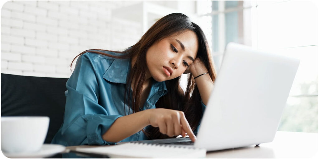 Woman on laptop bored at work, doing a tedious task 