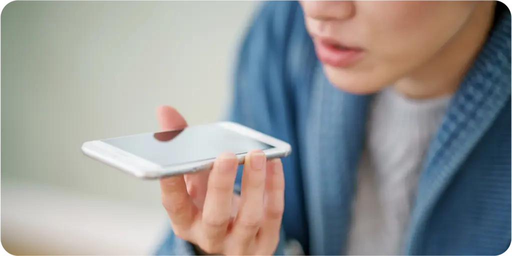 Image of a person speaking into a cell phone in their hand. 