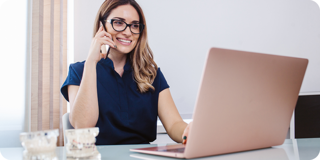 A woman in a navy blue shirt on the phone and looking at a laptop. 